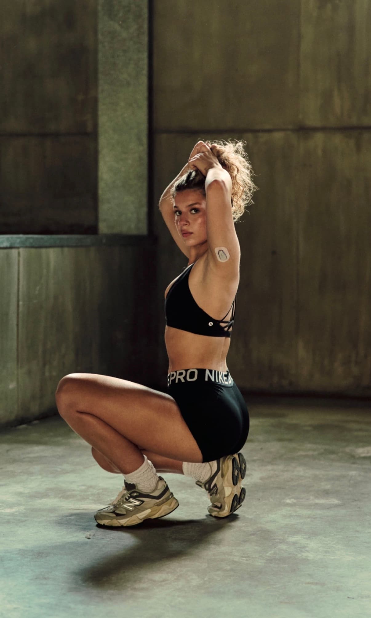 Monica, co-founder of Start Strong, crouching in workout gear in an industrial space.